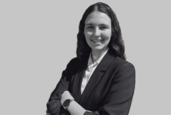 Professional woman in a blazer smiling with arms crossed in a grayscale headshot