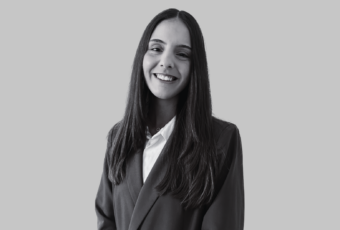 Smiling woman in a blazer and white blouse posing for a professional headshot against a gray background.